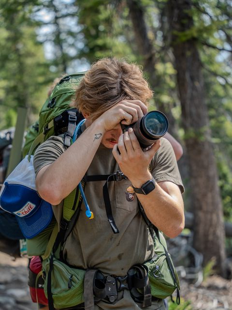 A backpacker raising a camera to take a photo on a forest trail
